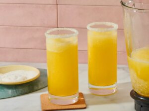 Two glasses of italian margaritas, a blender pitcher with similar contents nearby