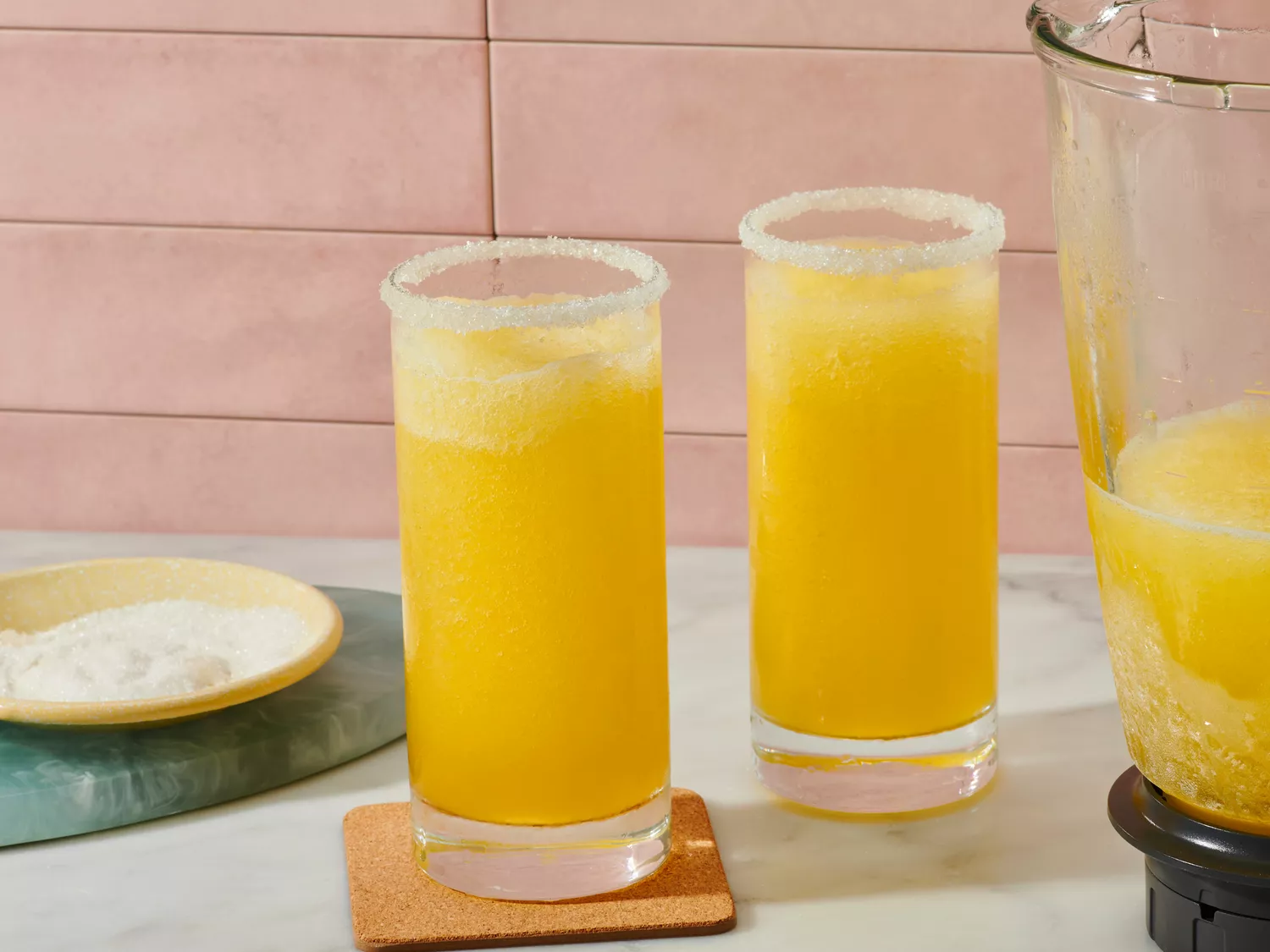 Two glasses of italian margaritas, a blender pitcher with similar contents nearby