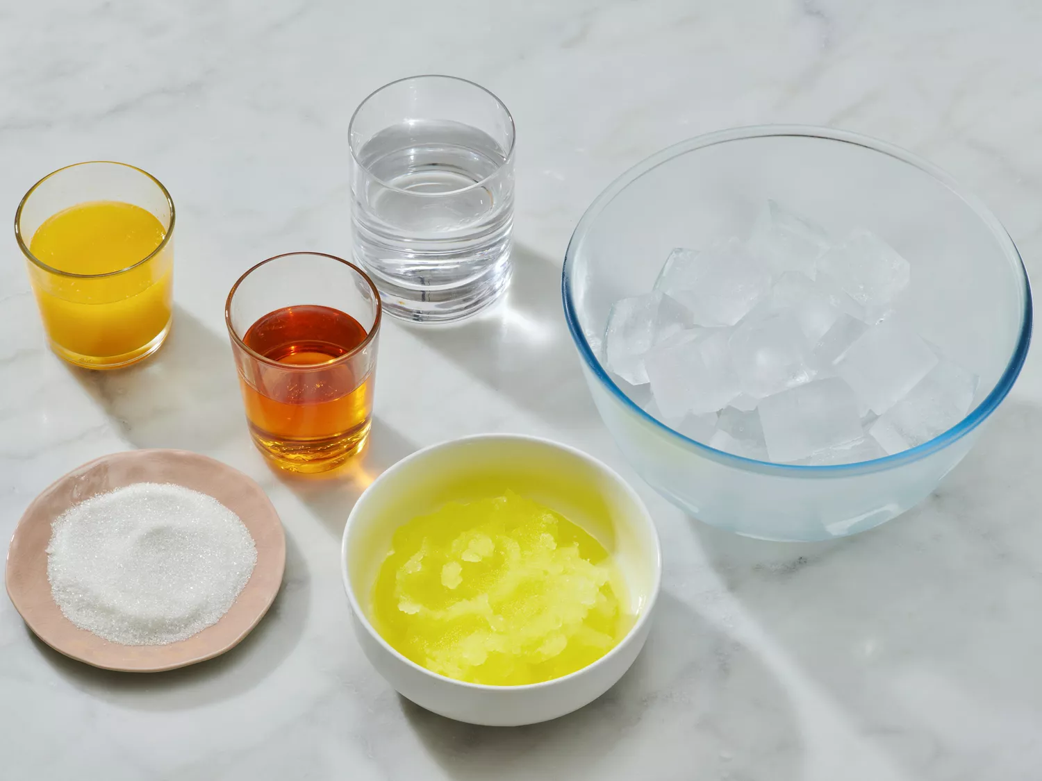 Ingredients for a beverage recipe arranged on a countertop, including liquids, sugar, and ice in a bowl