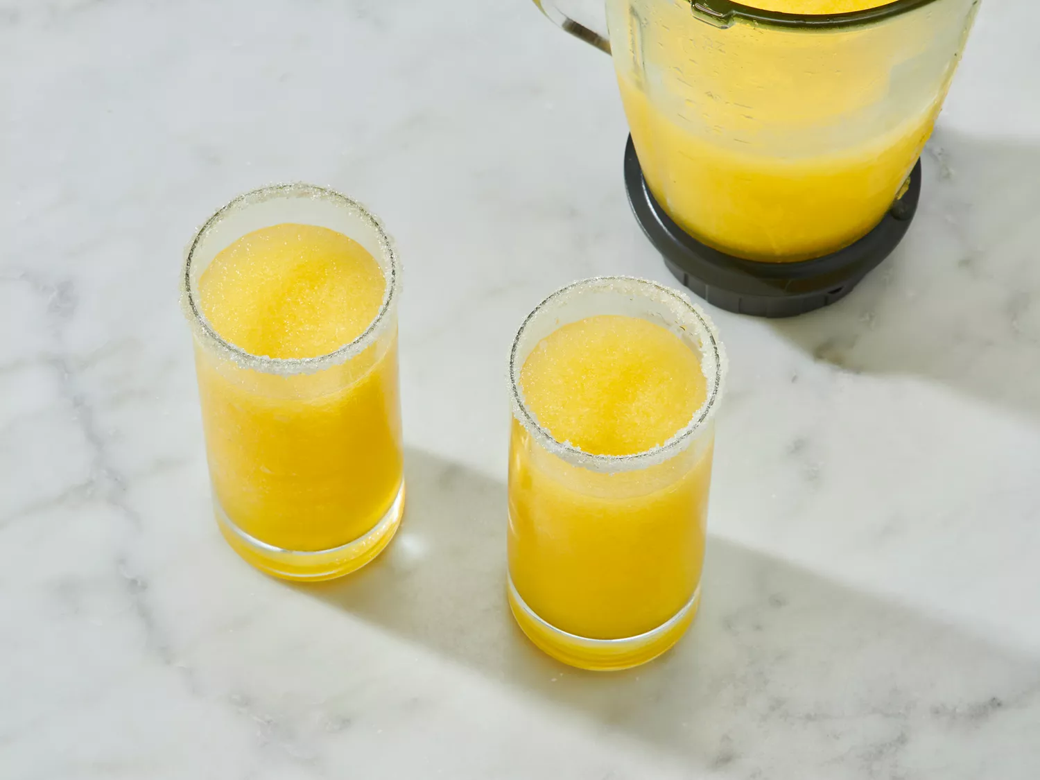 Two glasses of Italian Margaritas and a blender on a marble surface