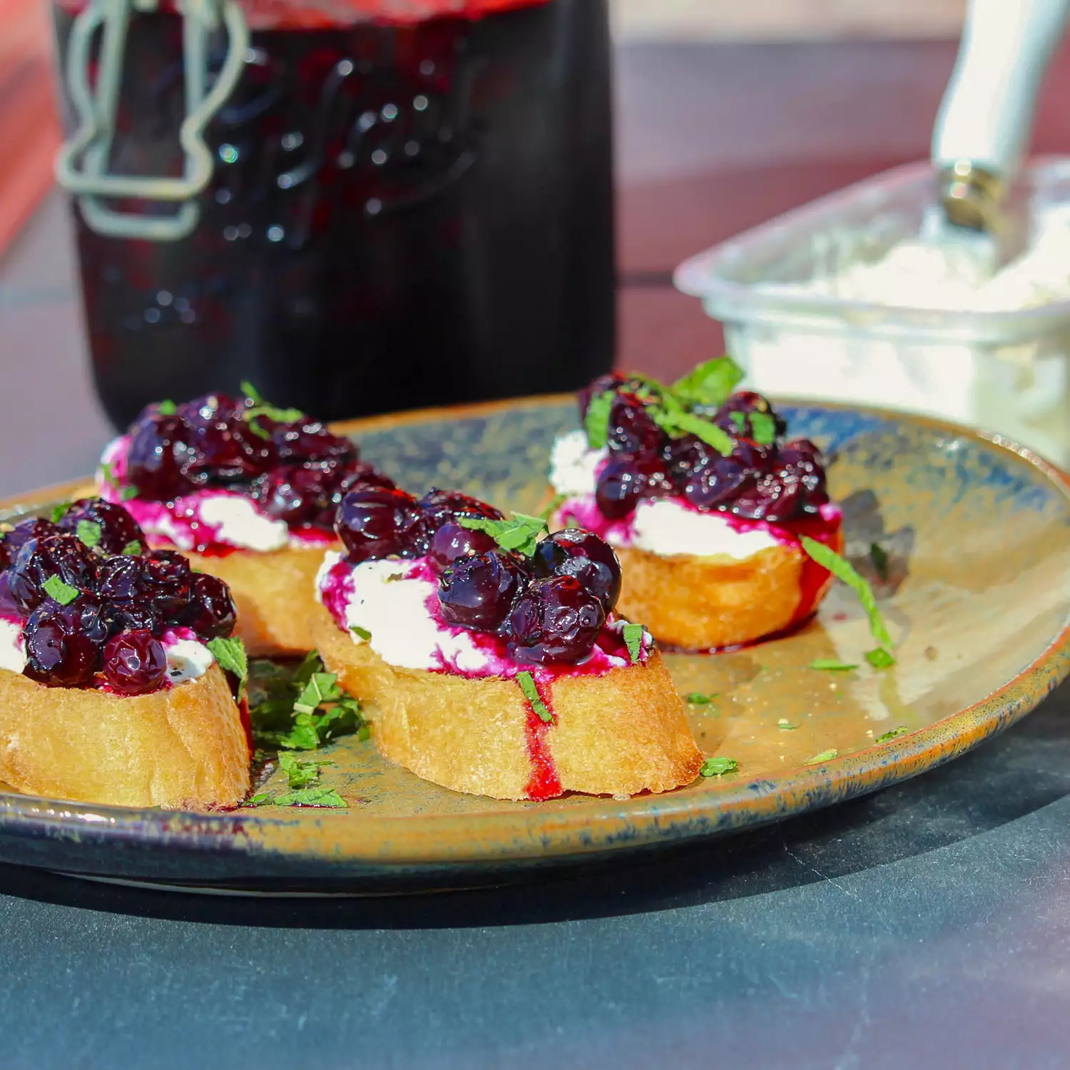 Close up view of pickled blueberries with cheese on bread, garnished with fresh herbs on a platter