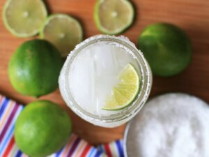 Overhead view of a keto margarita in a glass garnished with a lime wedge, with limes, lime slices and a bowl with salt in the background