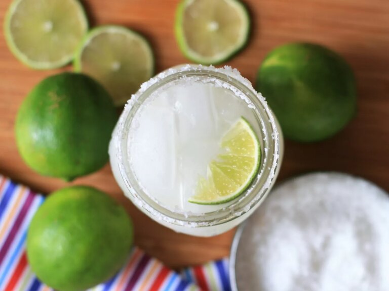 Overhead view of a keto margarita in a glass garnished with a lime wedge, with limes, lime slices and a bowl with salt in the background