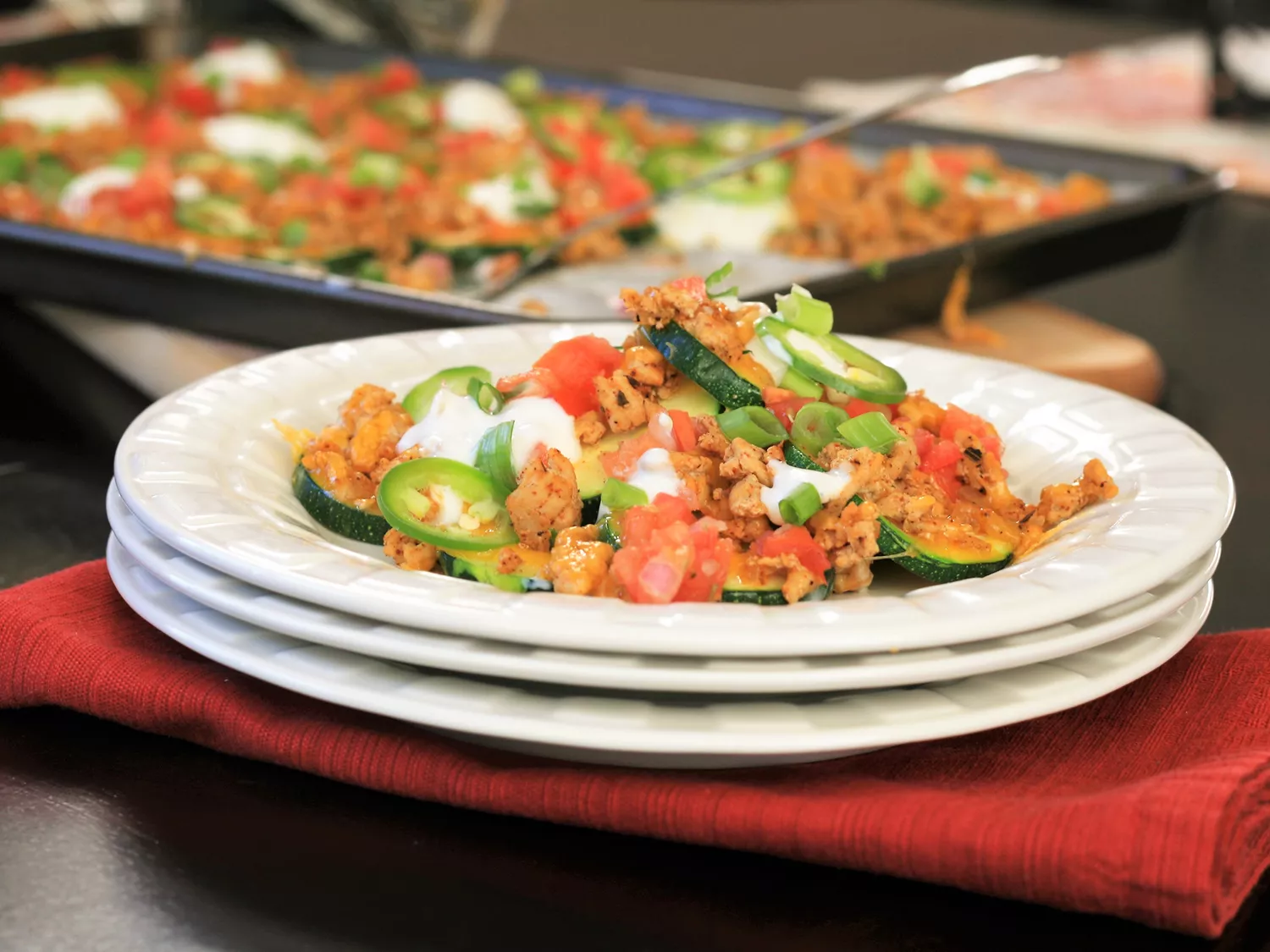 Close up view of zucchini nachos on a white plate and zucchini nachos in a baking dish with a serving spoon