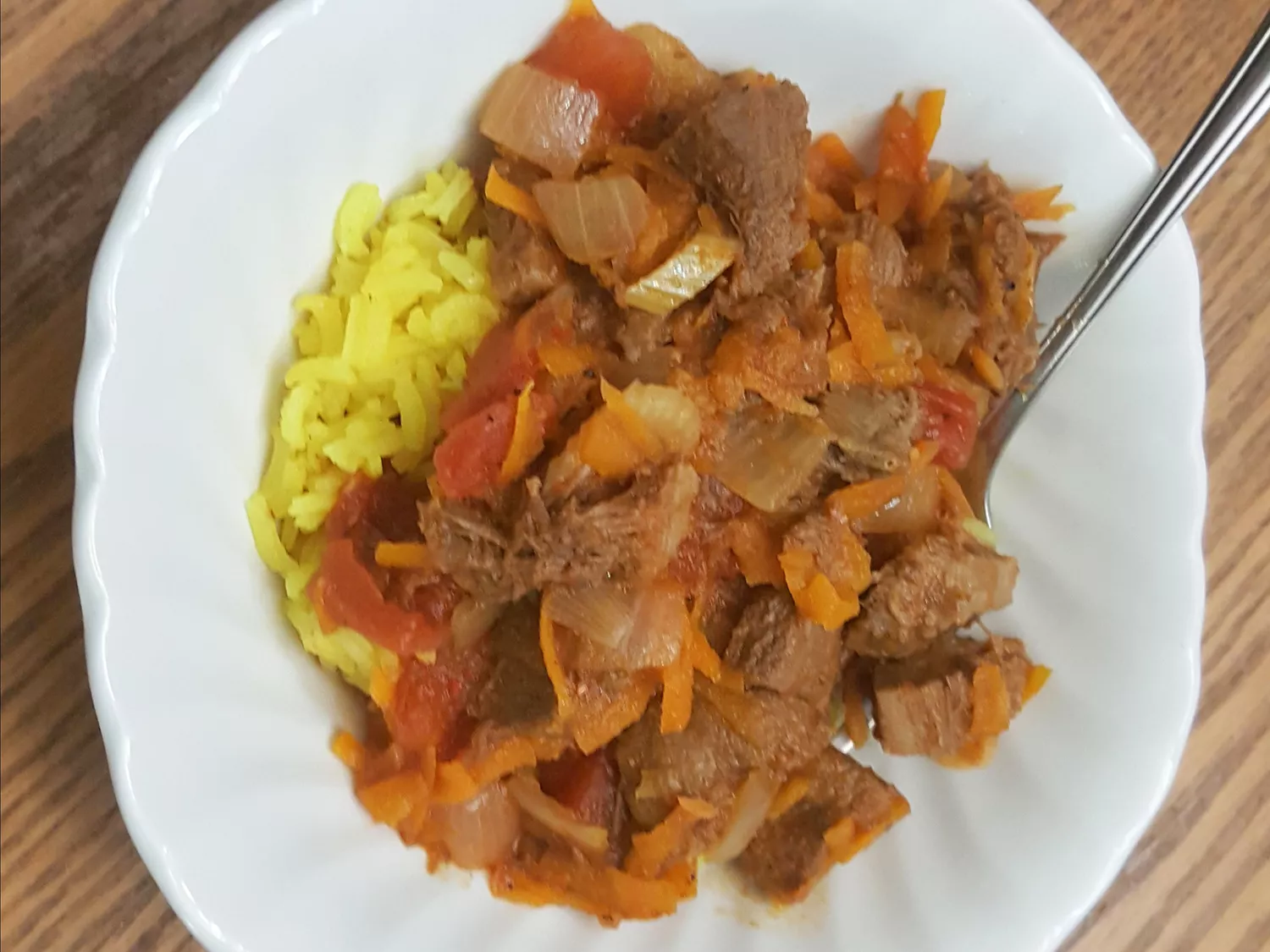 Close up view of lengua (beef tongue) stew with carrots, tomatoes and onions, served over rice, on a white plate with a fork
