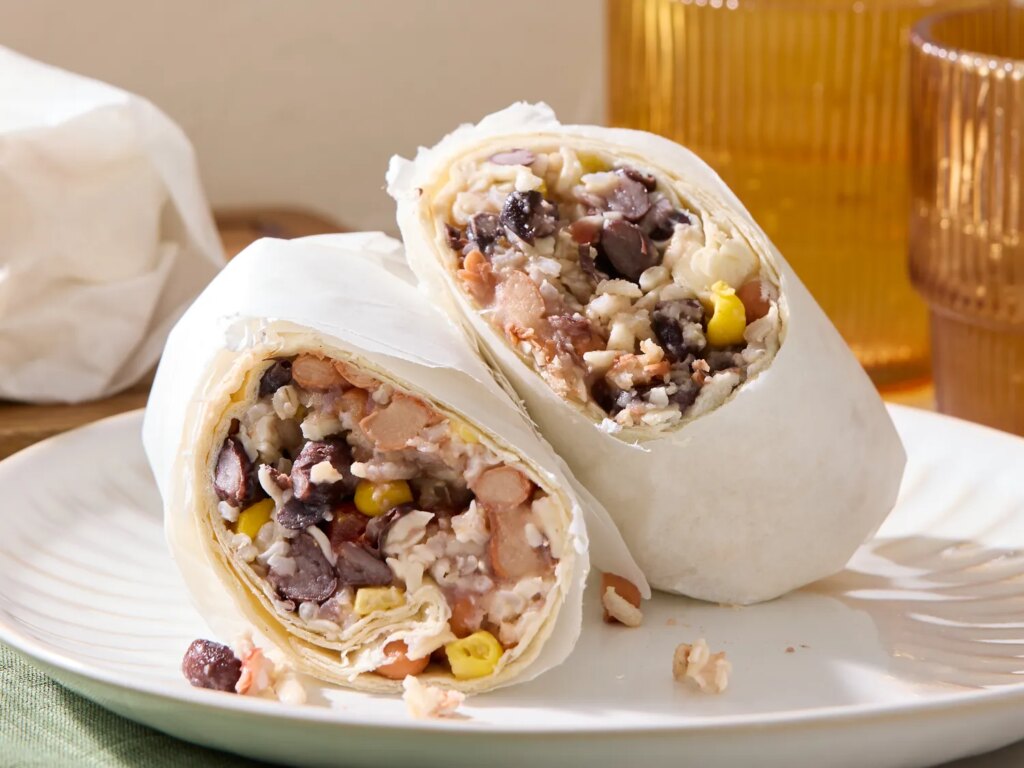 Two halves of a burritostyle wrap filled with beans rice corn and other ingredients placed on a white plate