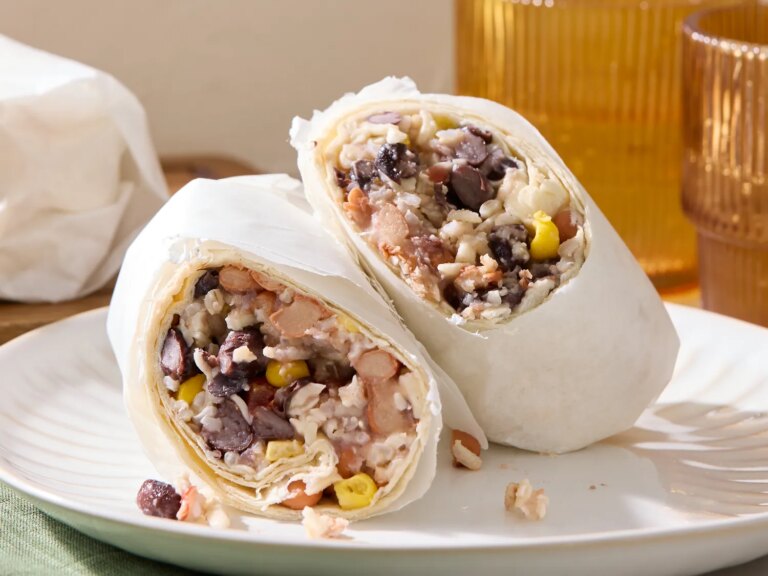 Two halves of a burritostyle wrap filled with beans rice corn and other ingredients placed on a white plate