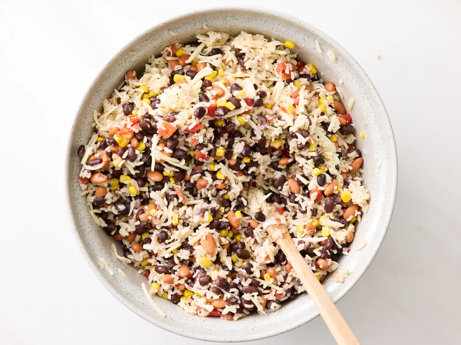 A bowl of rice mixed with beans corn and diced vegetables with a wooden spoon