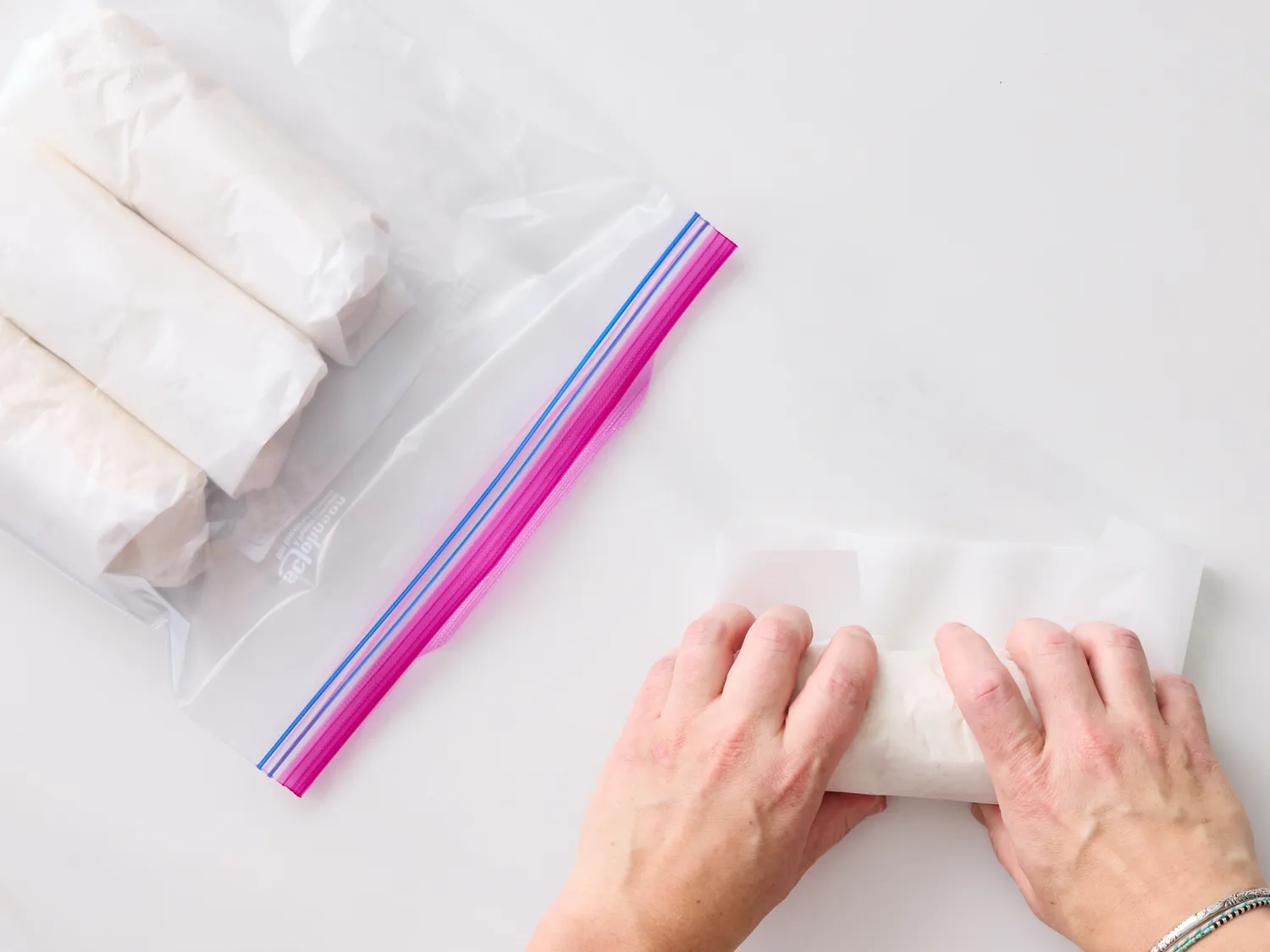 Hands wrapping a lunch wrap with plastic bags containing wraps visible on the side