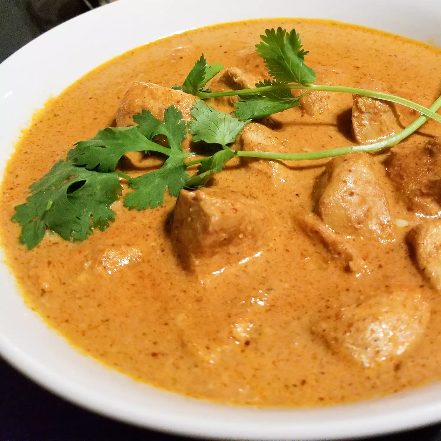 Close up view of makhani chicken (indian butter chicken) garnished with fresh herbs in a white bowl