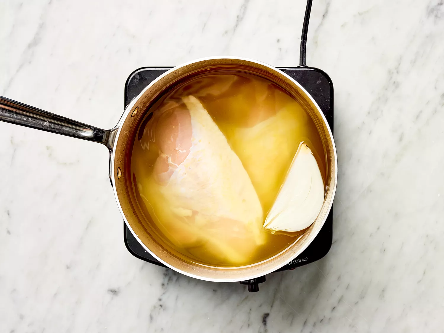 Chicken, broth, one quarter onion in a saucepan on a burner 