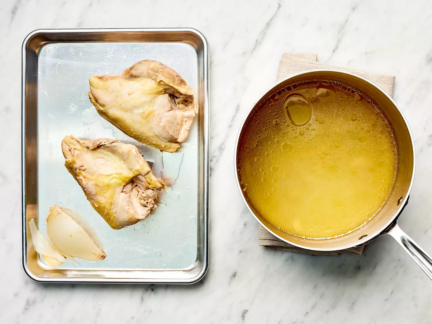 Chicken and onion on a baking sheet next to broth in a saucepan on a towel 