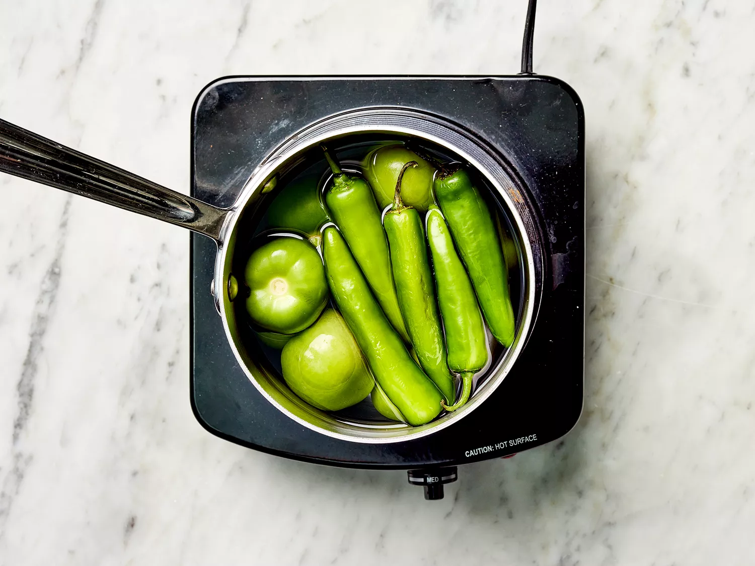 Tomatillos and serrano peppers with water in a saucepan on a burner 
