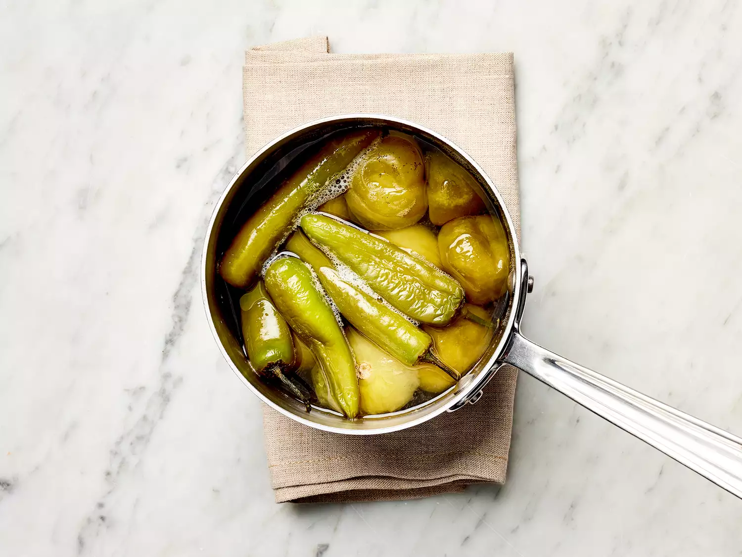 Tomatillos and serrano peppers with water in a saucepan on a towel