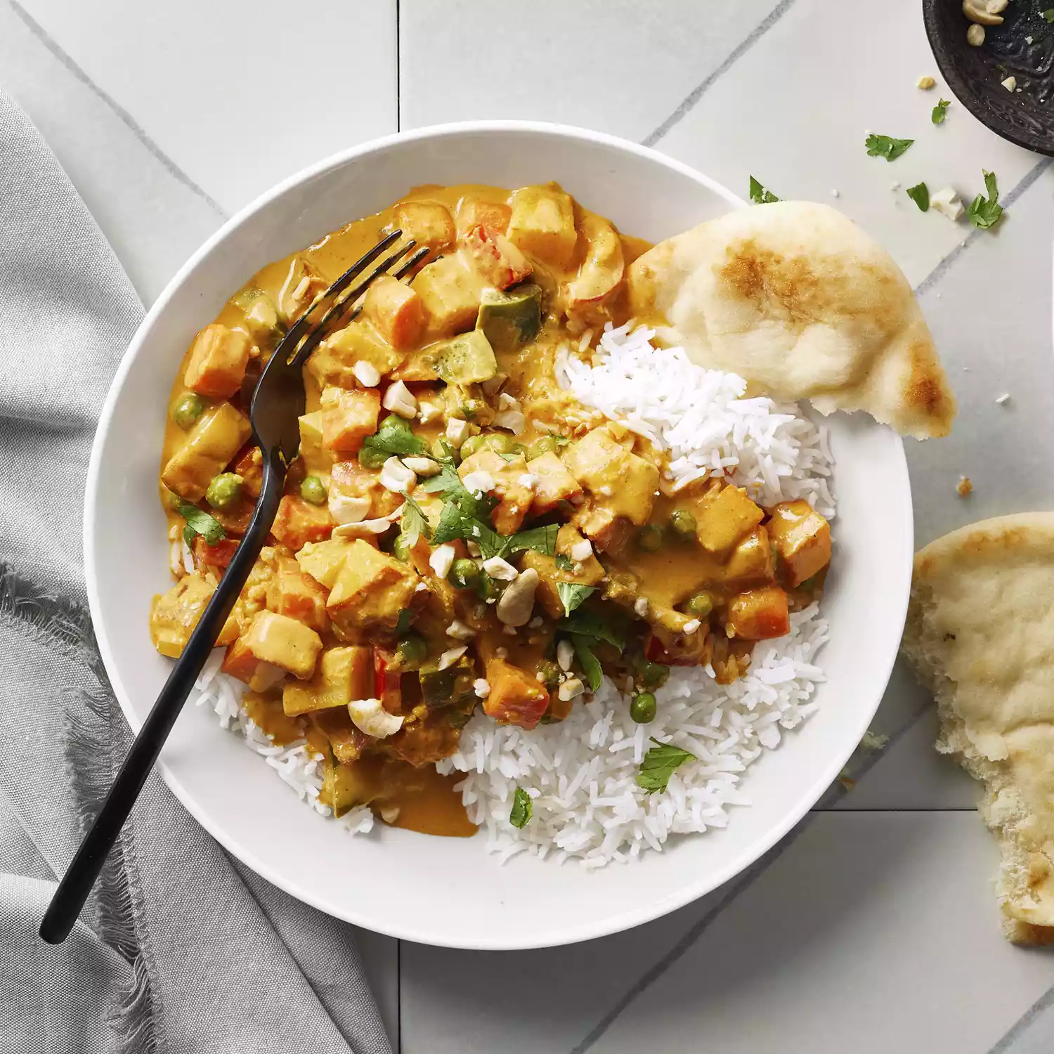 A white bowl of Vegetarian Korma served atop white rice and alongside Naan bread