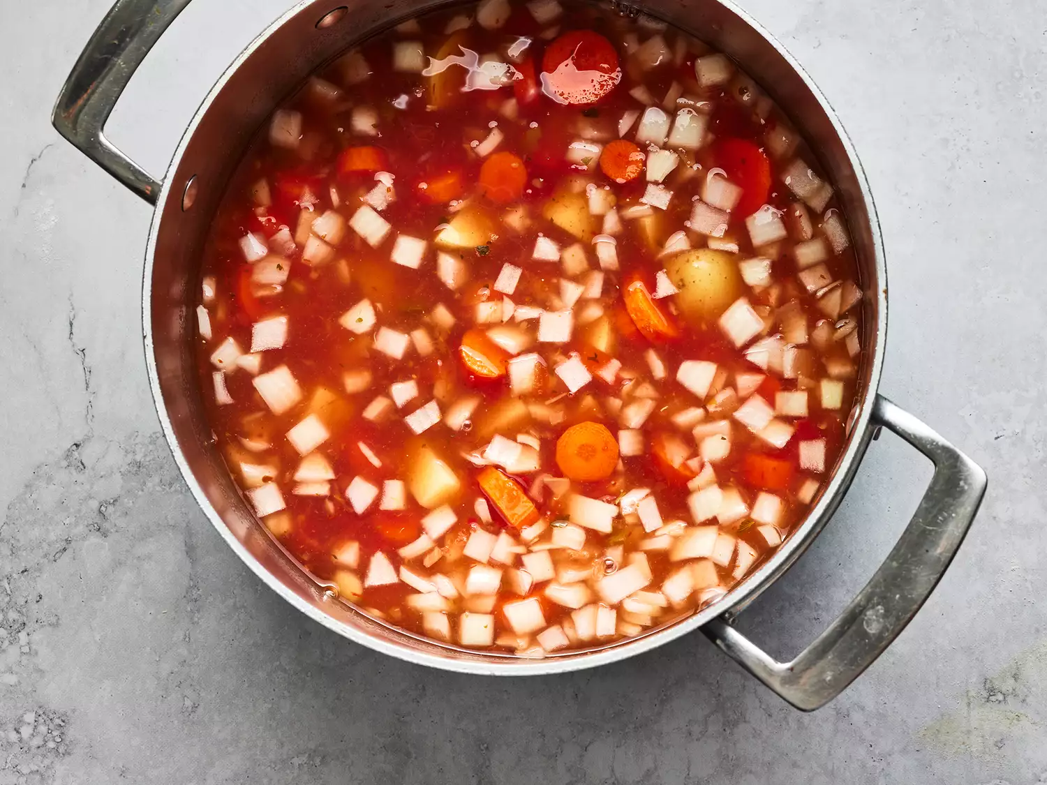Overhead shot of a pot with broth and vegetables cooking for albondigas