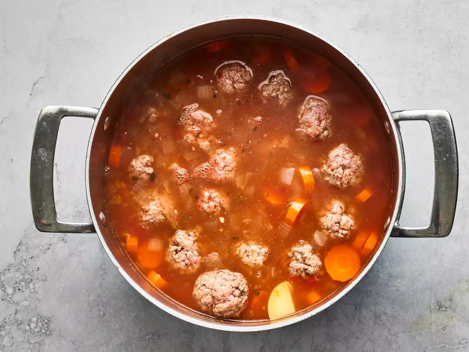 Overhead shot of meatballs and vegetables cooking in broth for albondigas soup