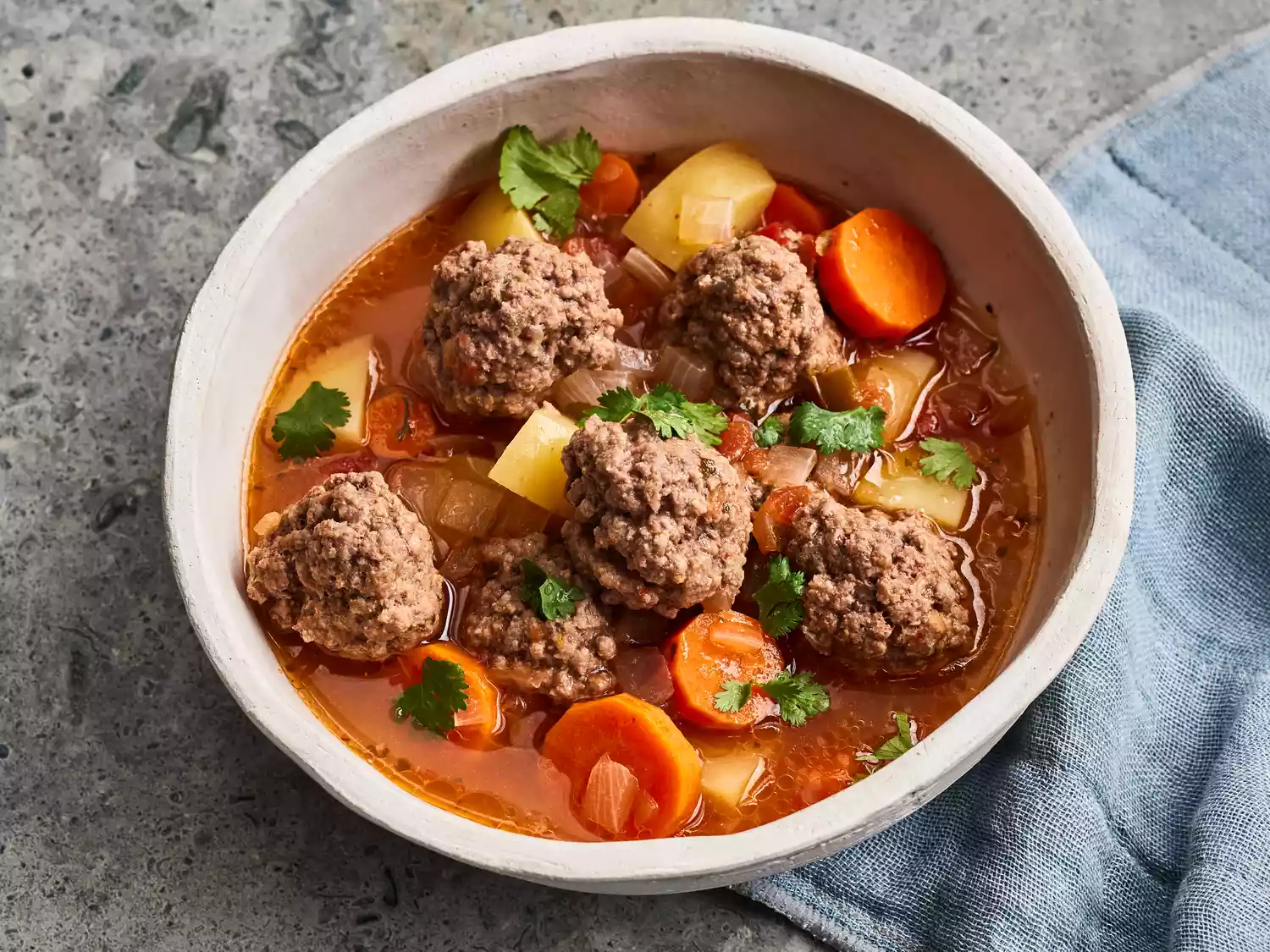 looking down at a large bowl of albondigas, with meatballs, carrots, potatoes and fresh herbs with broth
