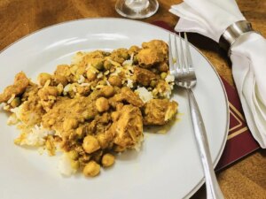Close up view of indian curried chicken thighs with white rice on a white plate with a fork
