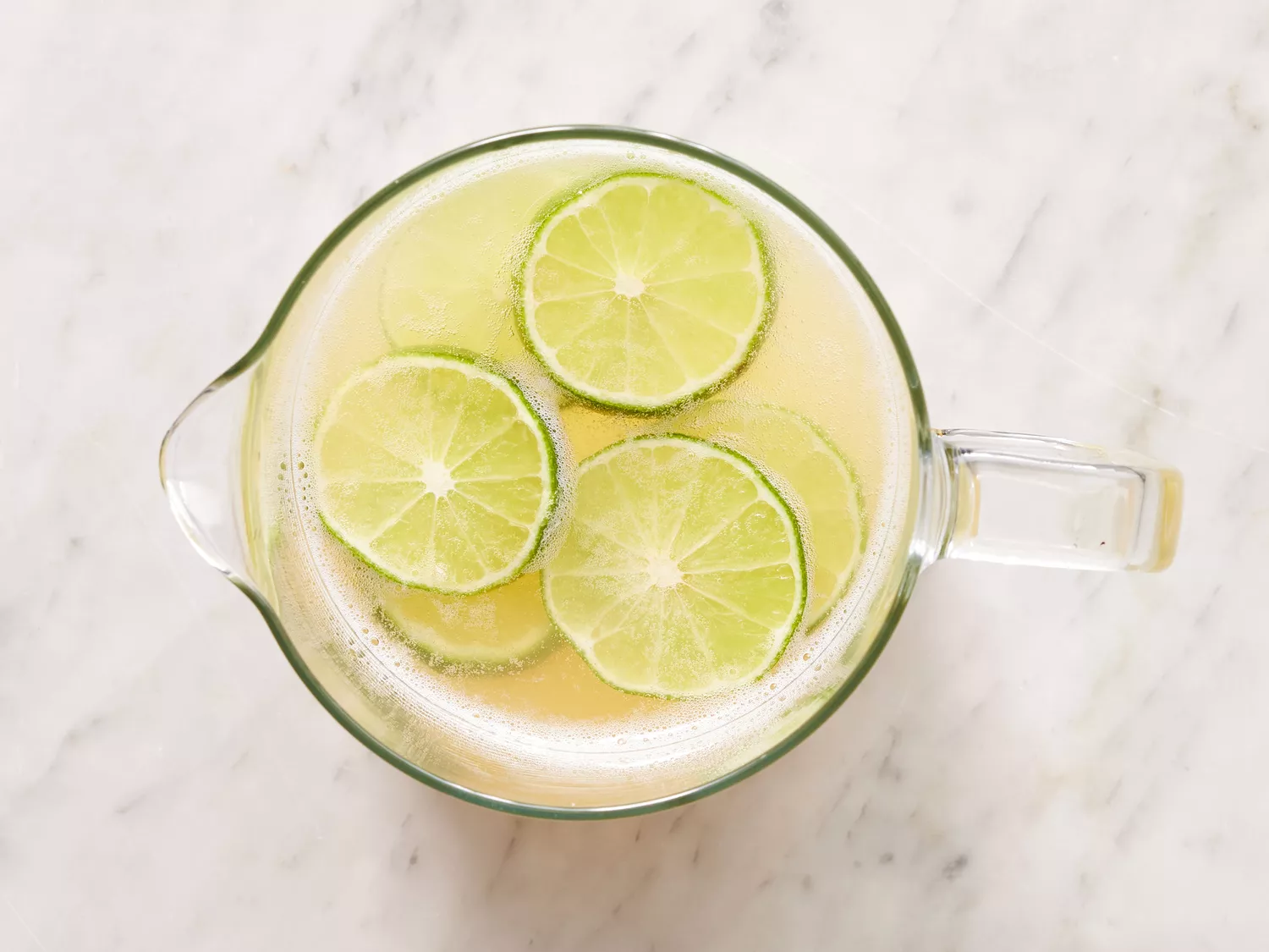 an overhead shot of limeade concentrate, tequila, water, and beer mixed with lime wheels in a pitcher