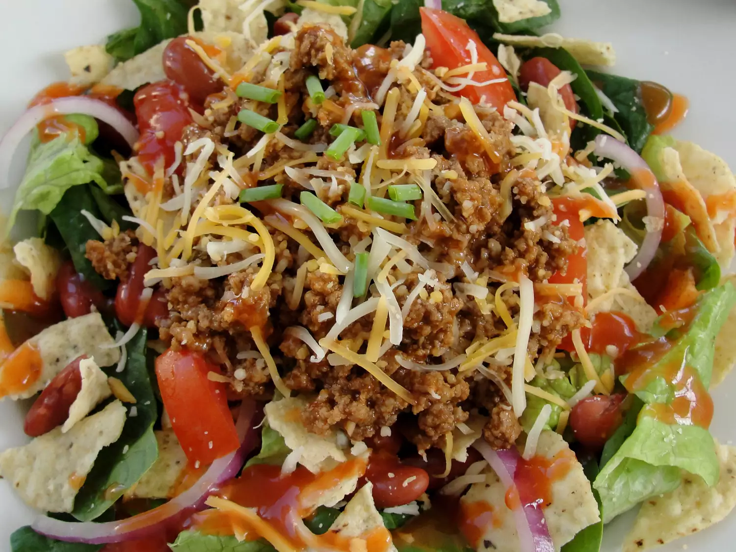 Close up view of taco salad garnished with cheese and green onions in a bowl