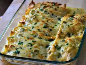 Close up view of chicken enchiladas with green chile sauce (salsa verde) in a glass baking dish