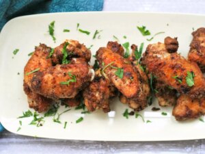Close up view of indian masala chicken wings garnished with fresh herbs on a white platter