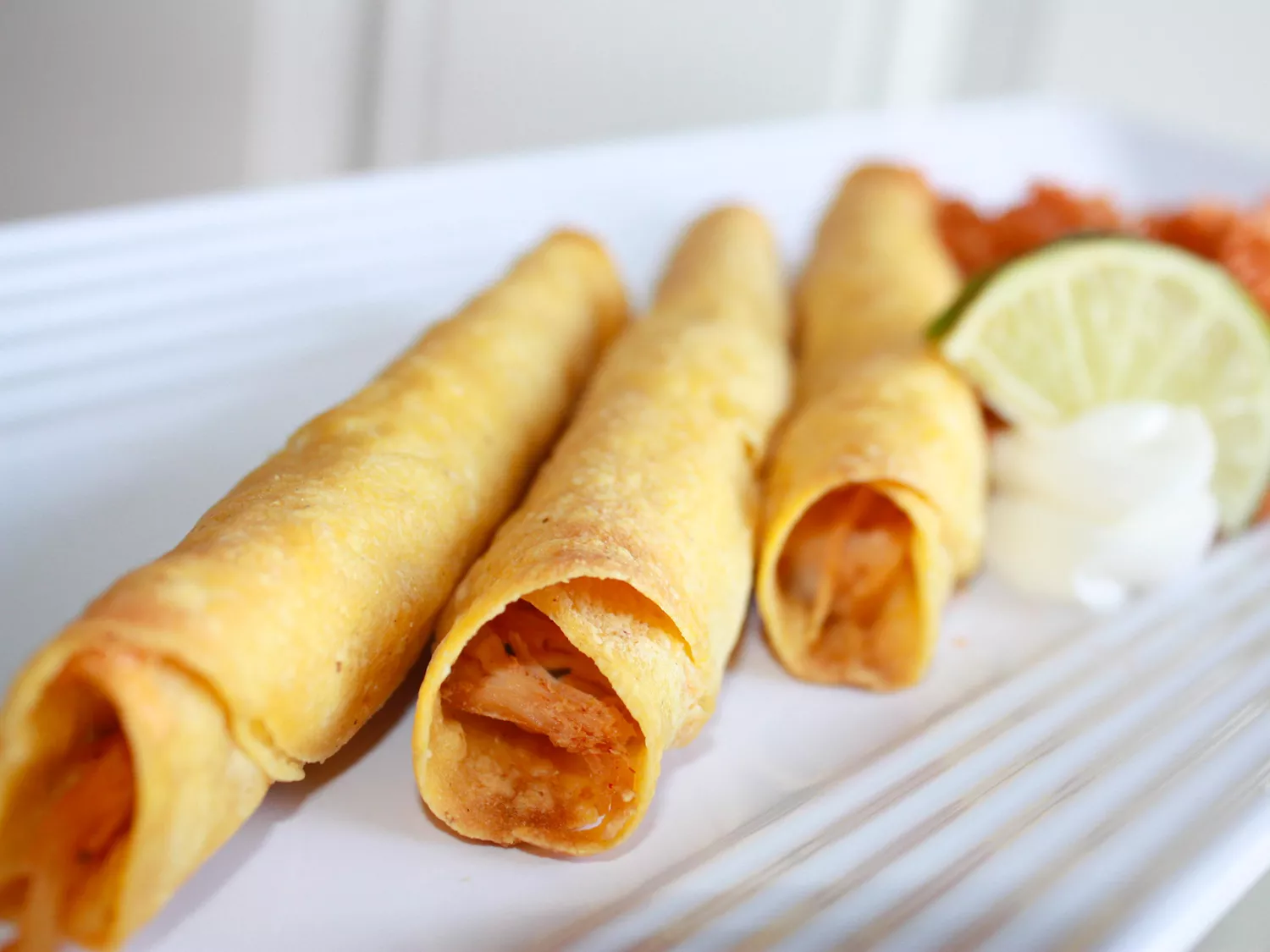 Close up view of chicken taquitos on a white platter with lime and salsa
