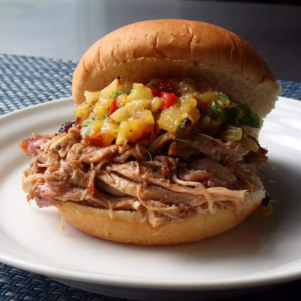 Close up view of pineapple pulled pork al pastor with pineapple relish on a bun, on a white plate