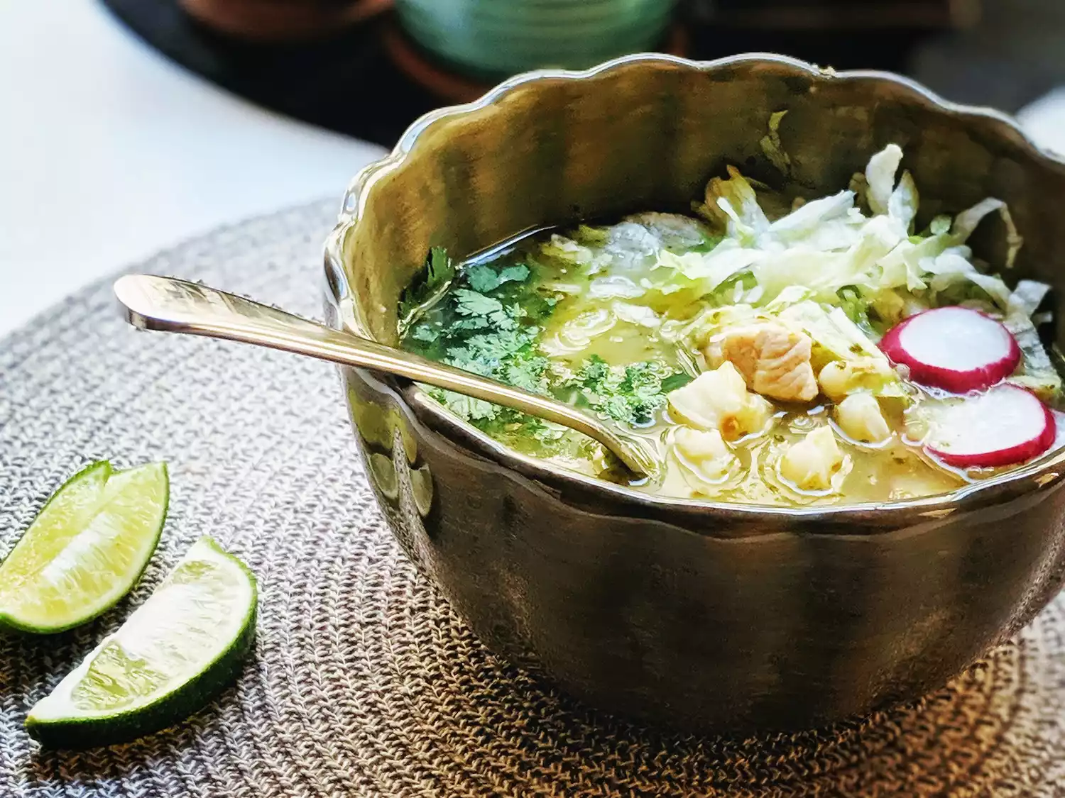 Close up view of instant pot chicken posole verde in a bowl with a spoon, served with lime wedges