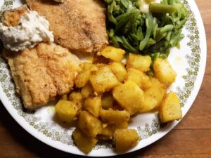 Close up view of bombay potatoes served with fish and vegetables on a plate