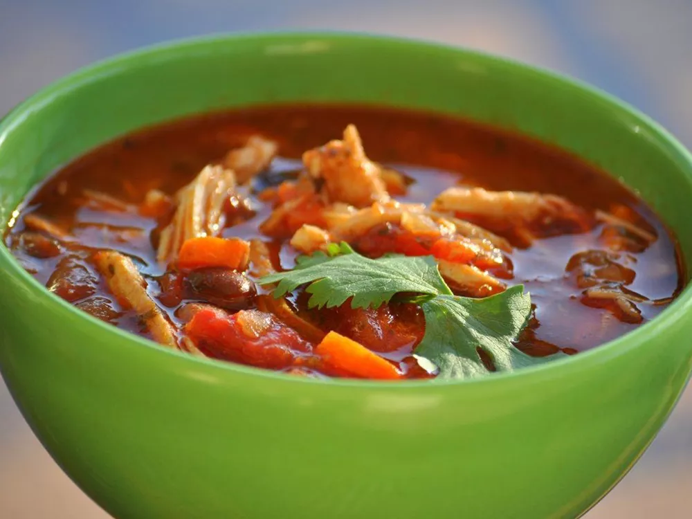 Closeup of catherine's spicy chicken soup in a green bowl garnished with a cilantro sprig