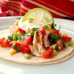 Close up view a fiery fish taco with crunchy corn salsa garnished with a lime wedge on a plate