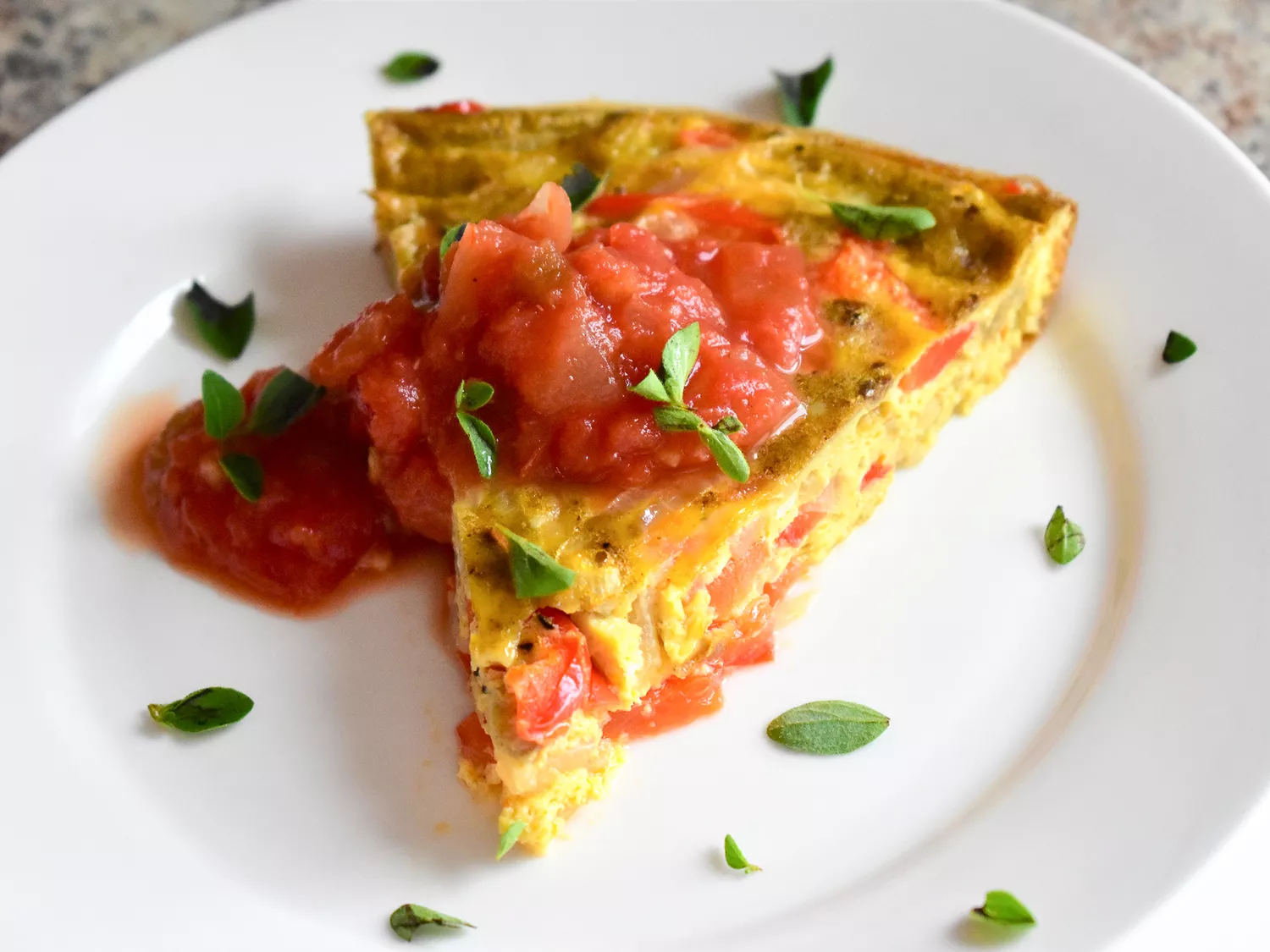Close up view of a slice of mexican frittata garnished with salsa and fresh herbs on a white plate
