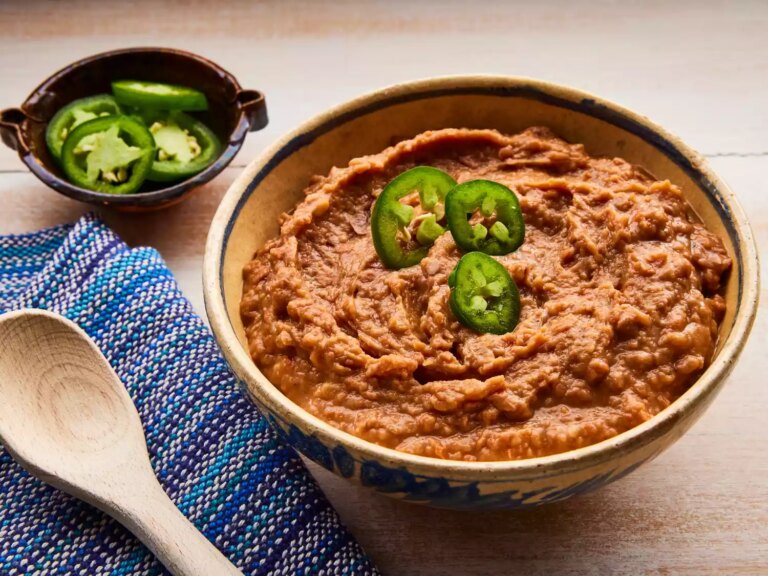 Close up on a bowl of refried beans without the refry, garnished with a few jalapeño slices.