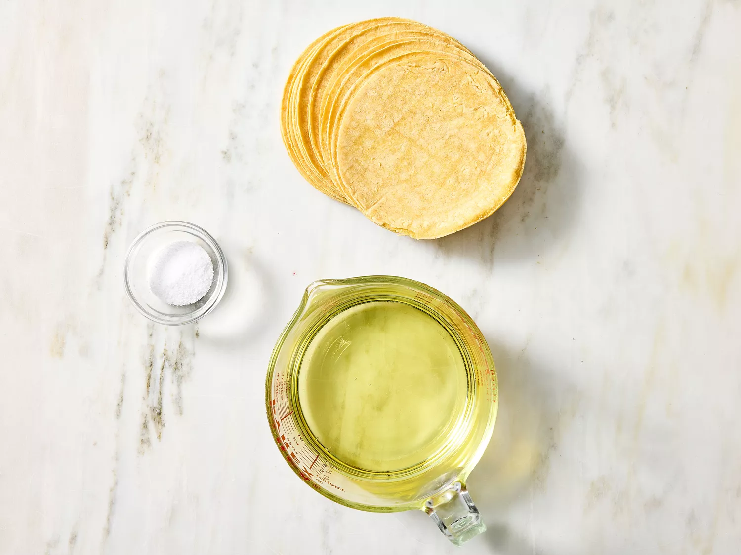 Corn tortillas, oil, and salt set out for making taco shells.