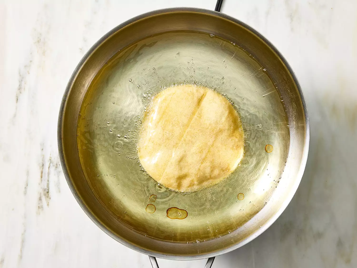Corn tortilla frying in oil to create taco shell.