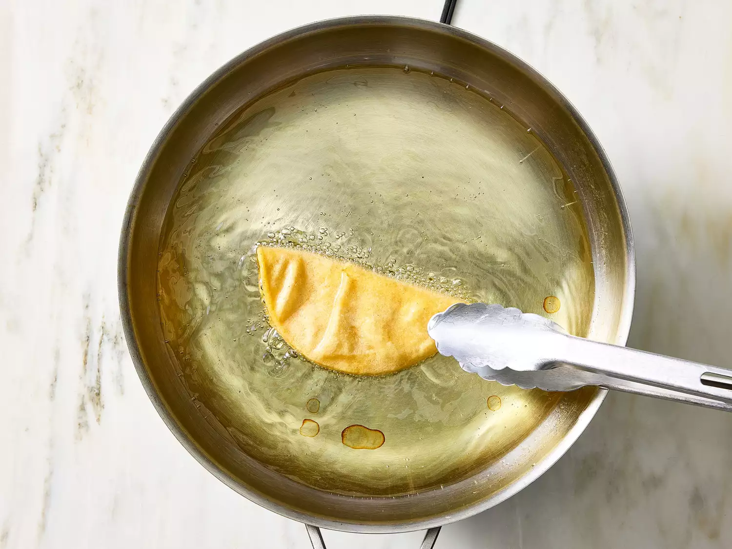 Corn tortilla frying in oil to create taco shell.