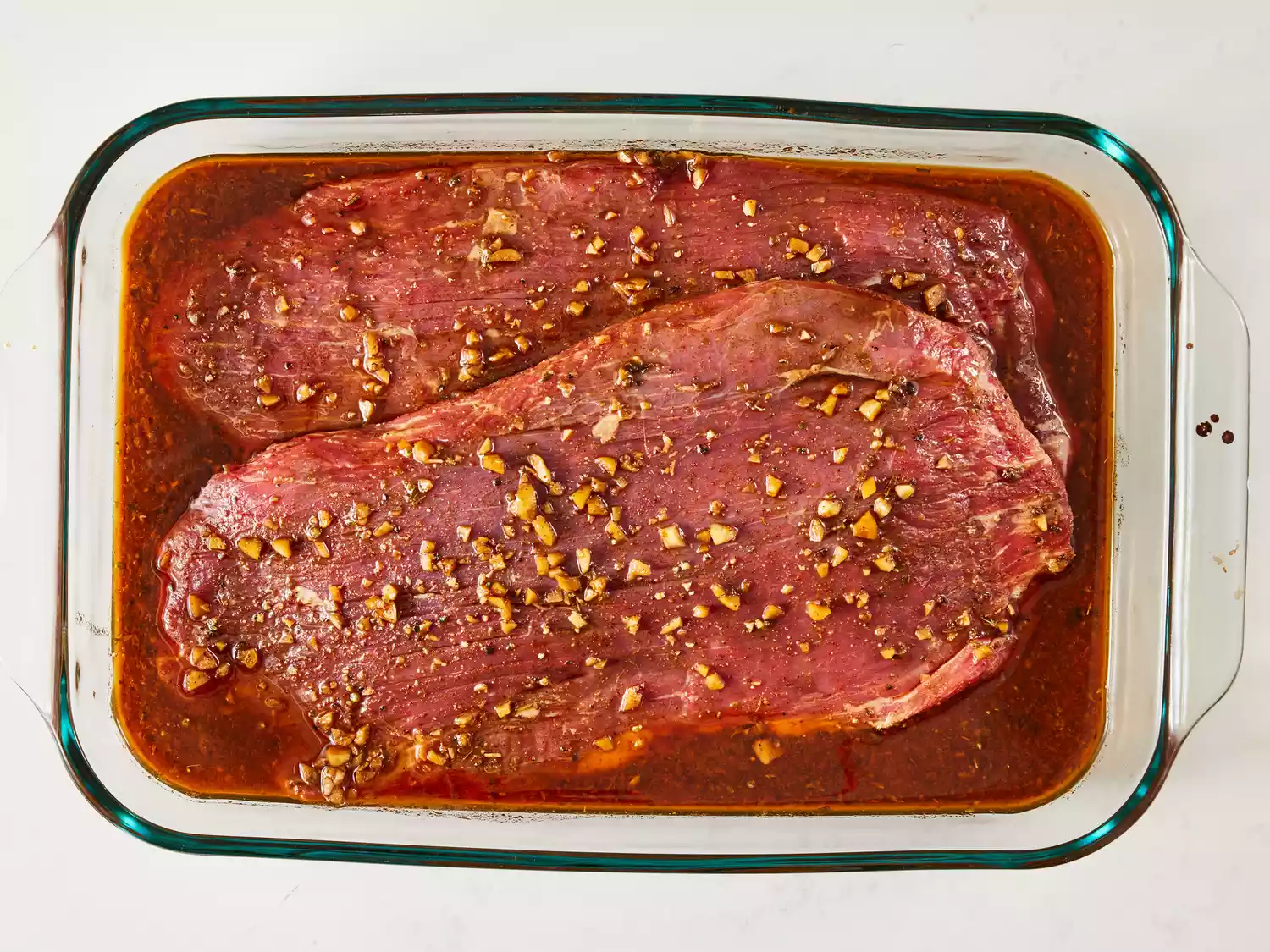 an overhead shot of flank steak laid in marinade in a glass baking dish 