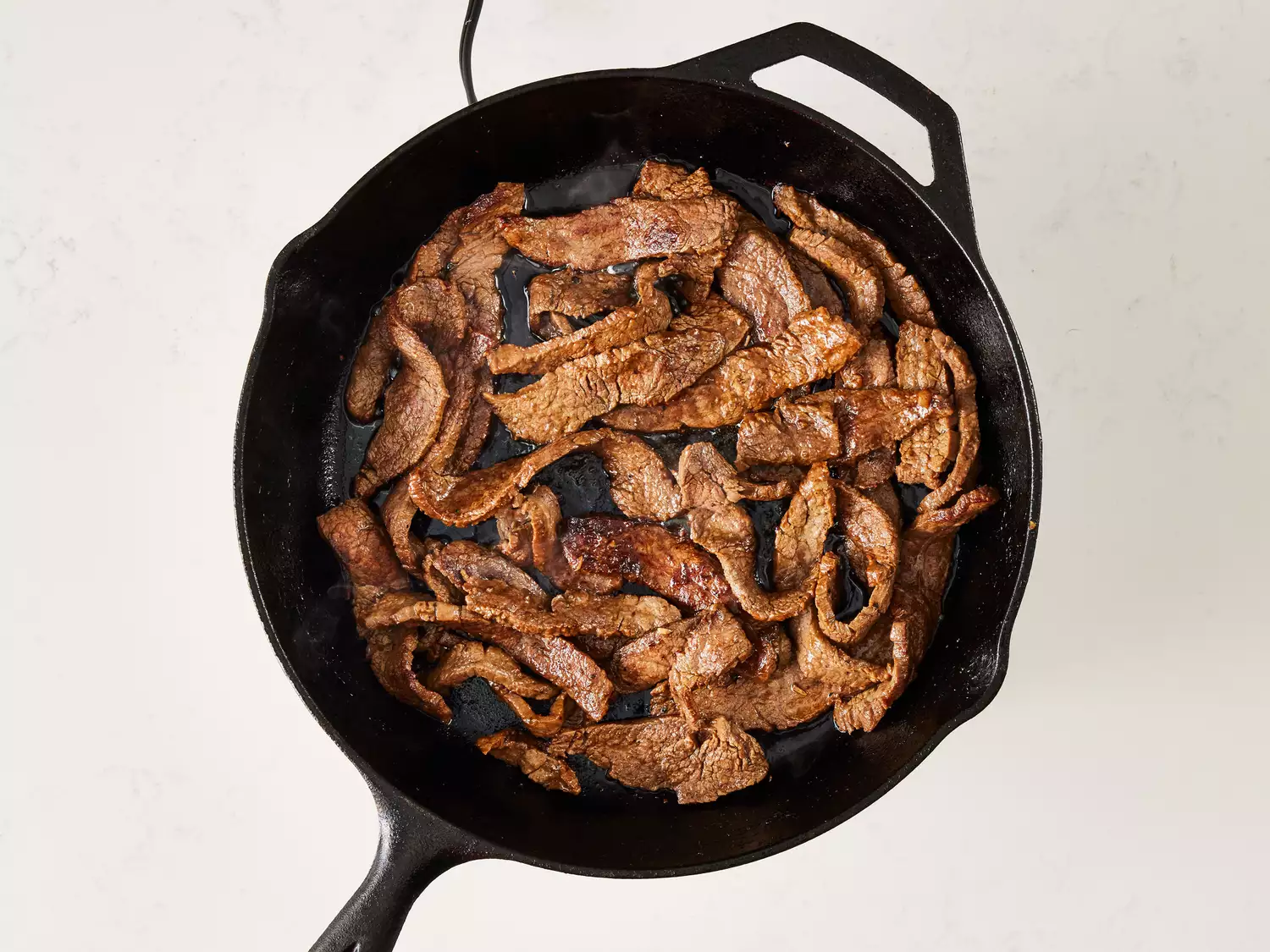 an overhead shot of sliced flank steak cooking in a cast iron skillet 