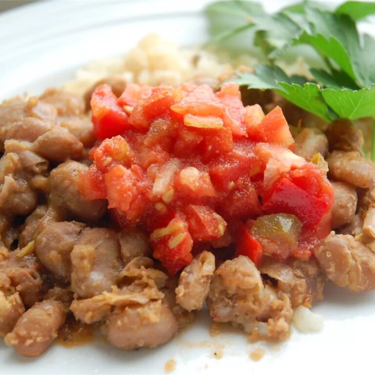 Close up view of pinto beans garnished with salsa and fresh herbs on a white plate