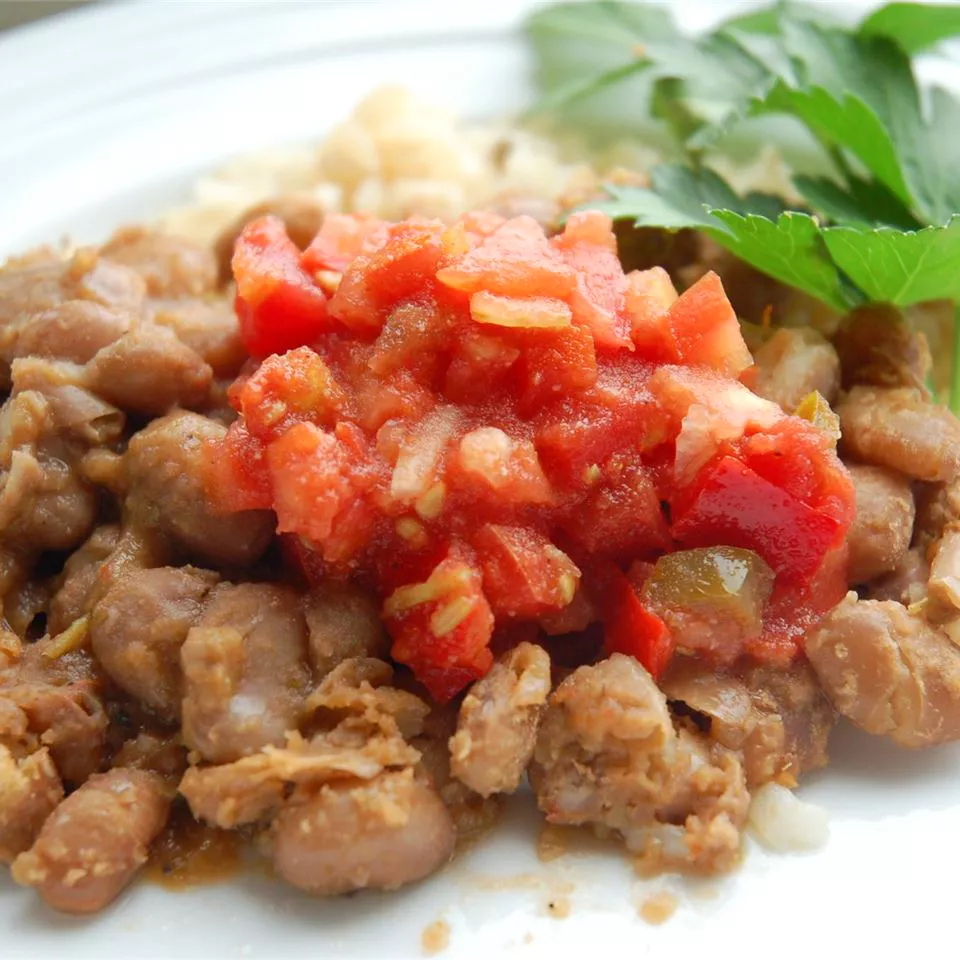 Close up view of pinto beans garnished with salsa and fresh herbs on a white plate