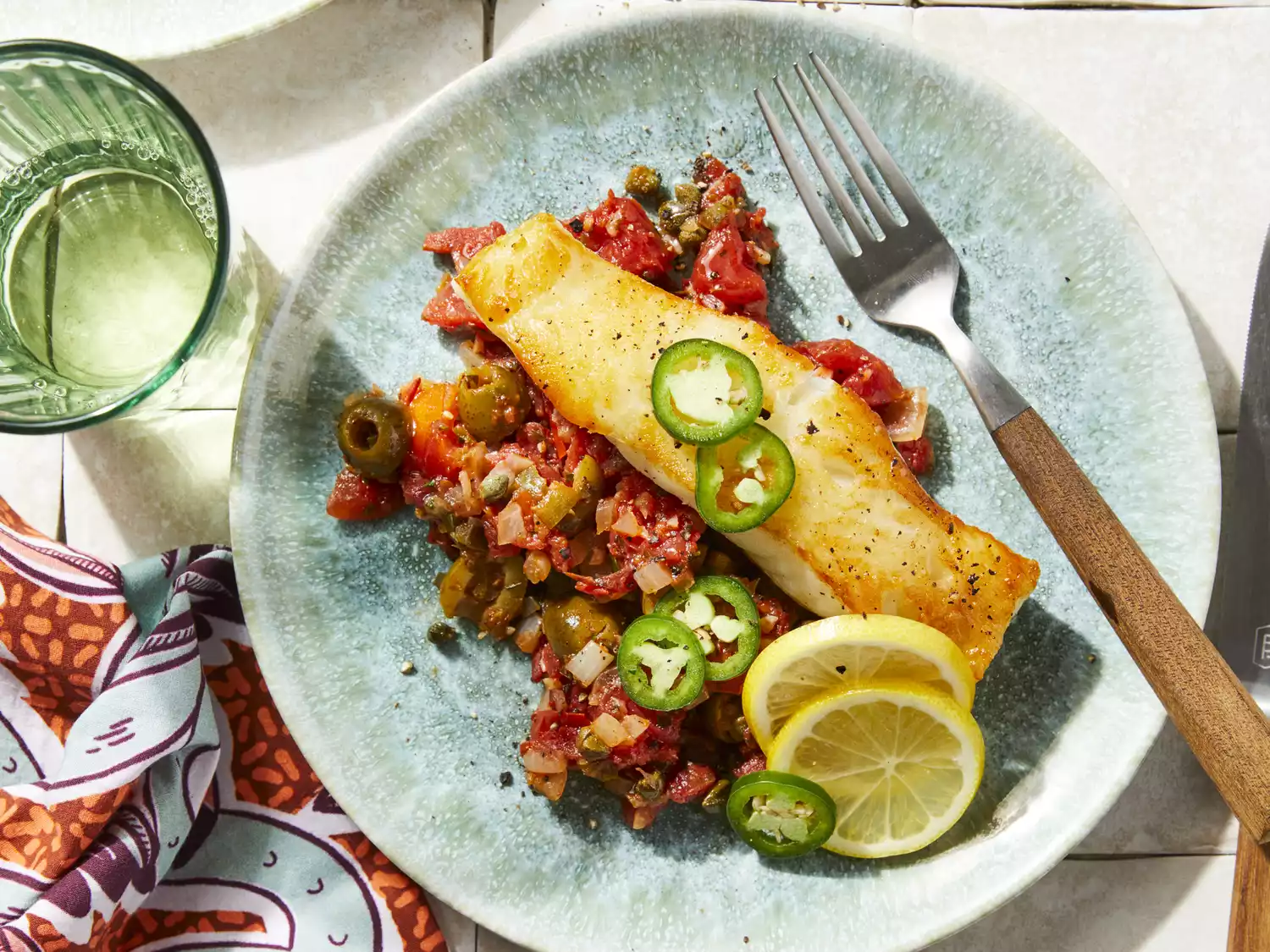 White fish fillet with jalapeno slices on top of olive salsa with slices of lime