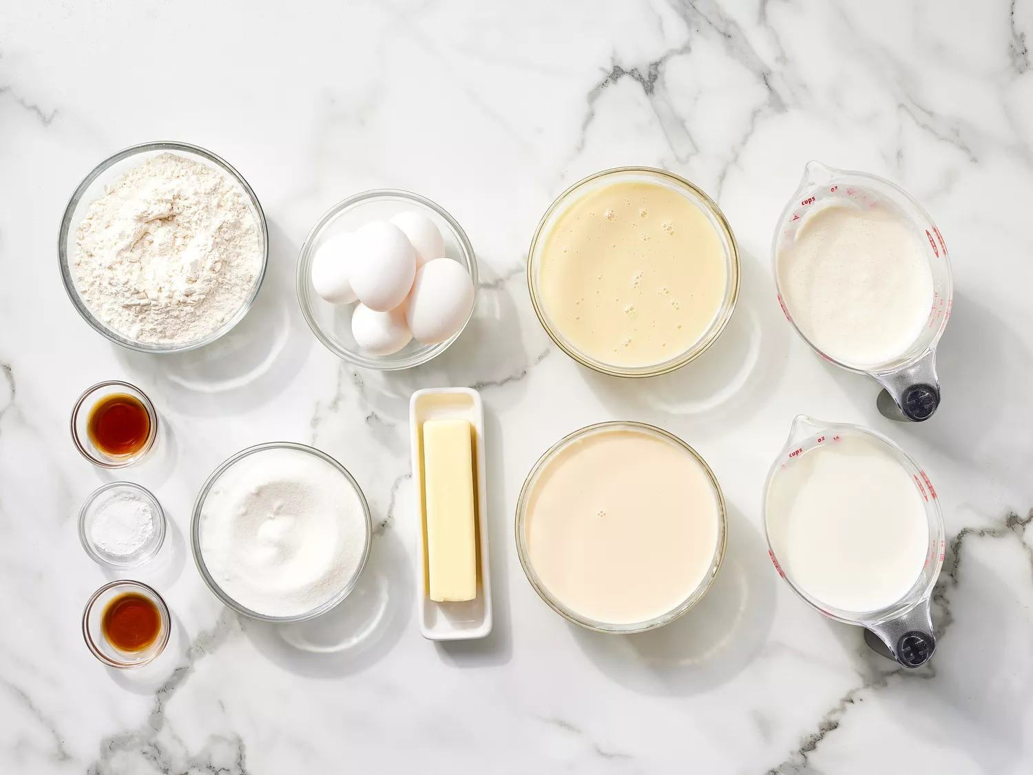 Tres Leches (Milk Cake) ingredients in glass bowls on a marble counter 