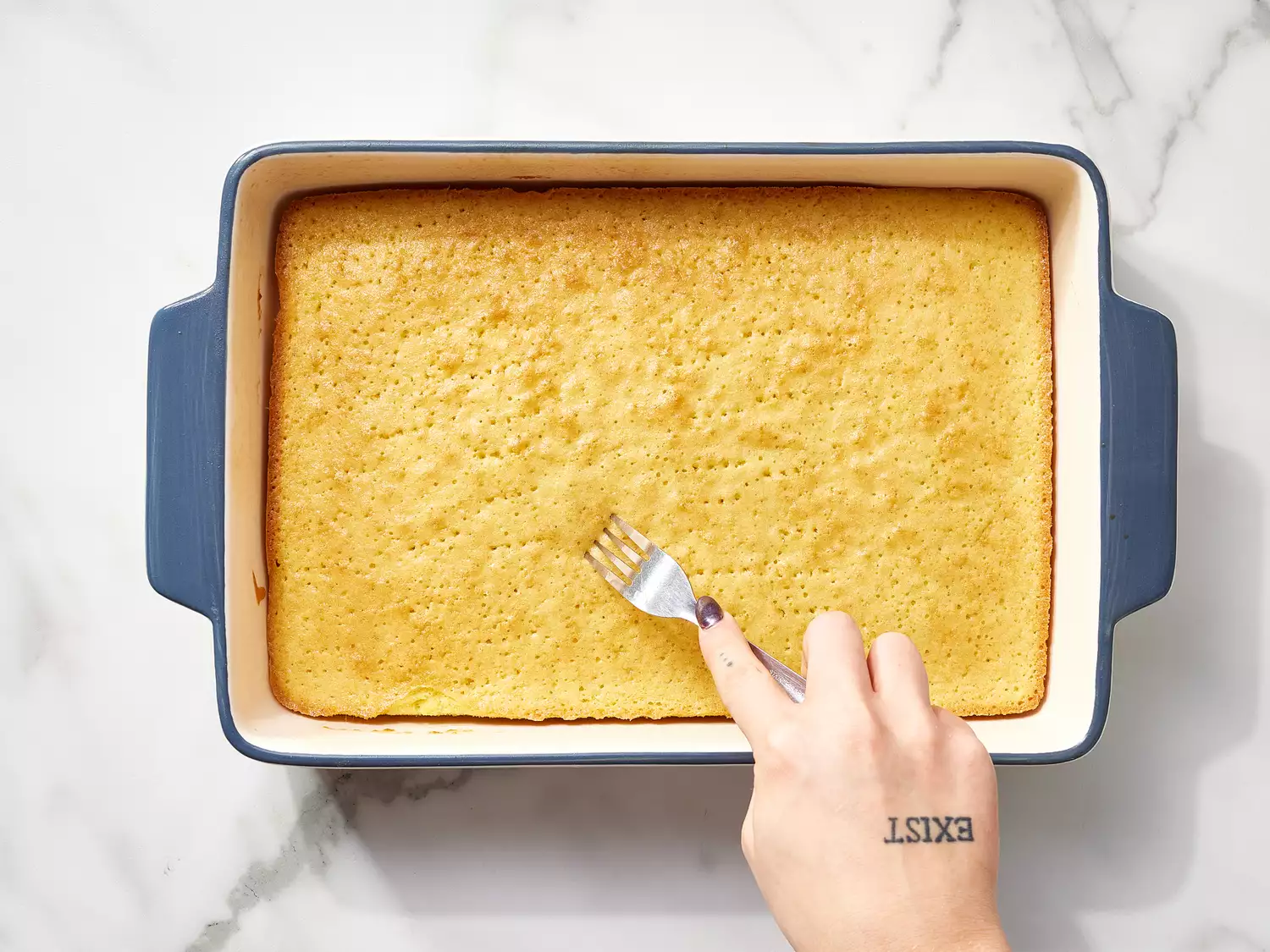 Hand using a fork to poking holes in a cake in a baking dish 