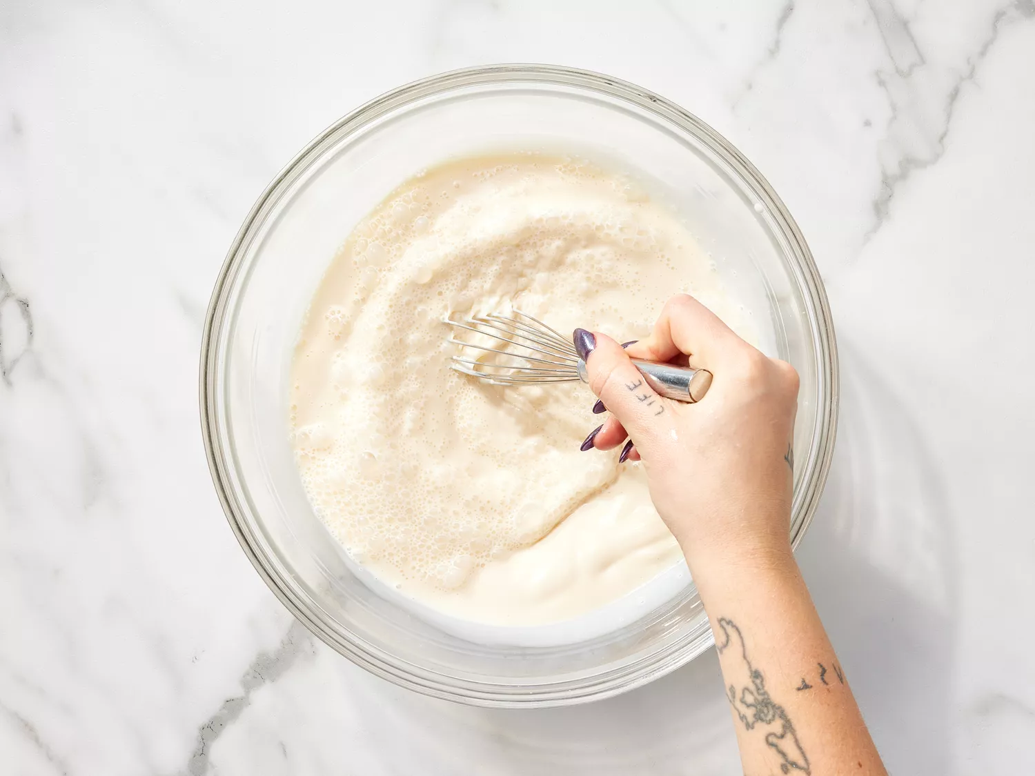 Hand whisking whole milk, condensed milk, and evaporated milk together in a glass bowl