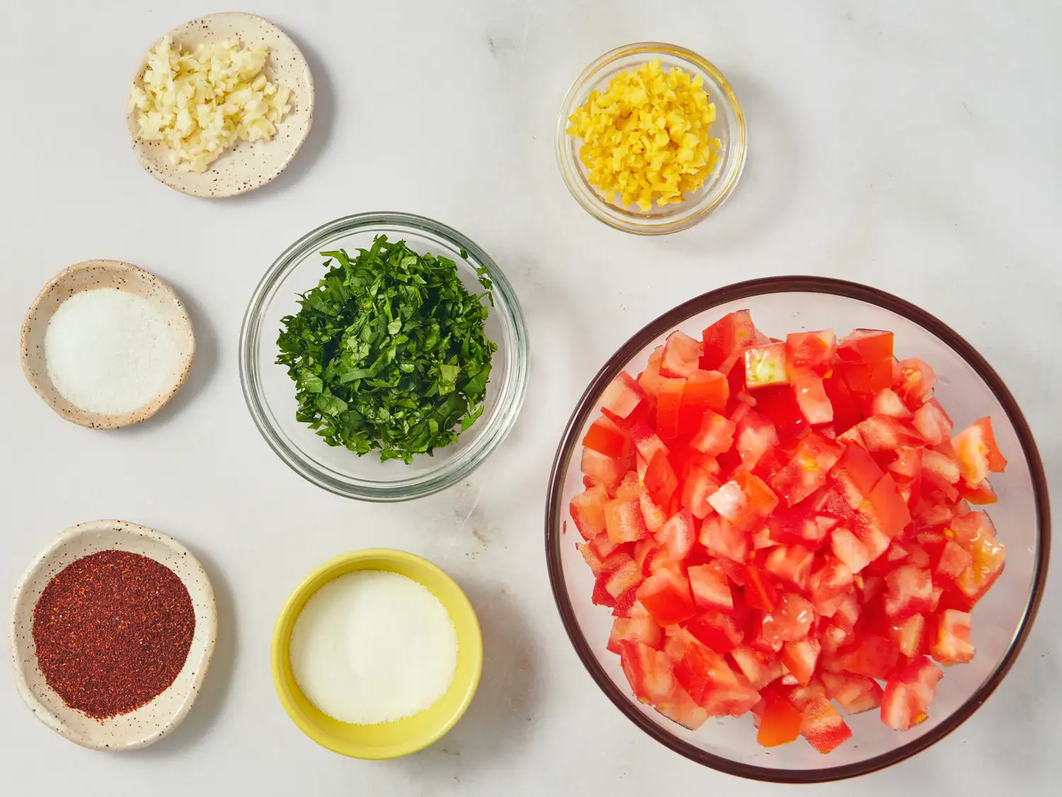 Ingredients including chopped tomatoes chopped herbs and spices arranged for a recipe preparation