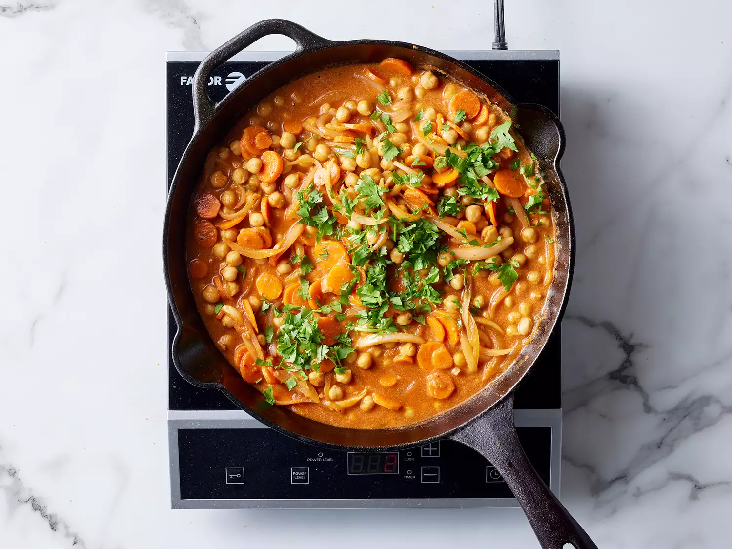 Fresh cilantro added to chickpea tikka masala in a cast iron skillet. 
