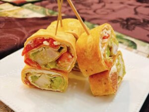 Closeup of stack of tortilla wrap appetizers held together with toothpicks on white plate with patterned tablecloth in background
