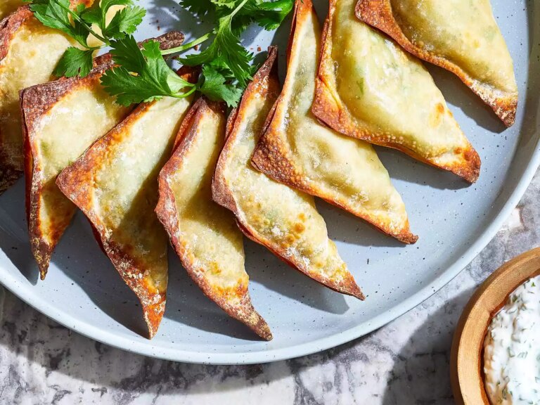 A close up, overhead view of a platter of neatly arranged air fryer samosas, served with a yogurt cilantro dipping sauce.